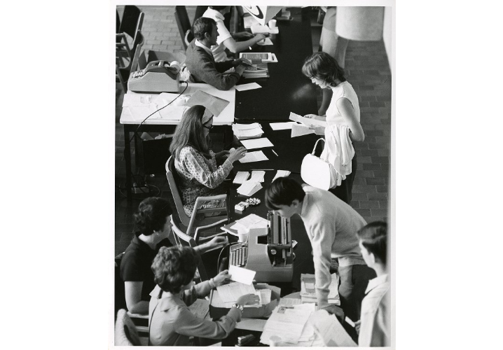 A photograph of students crowded around tables filled with forms and typewriters, likely for course enrollment. Photo sourced from the UTSC Photographic Services Collection: https://collections.digital.utsc.utoronto.ca/islandora/object/photoservices%3A549. 